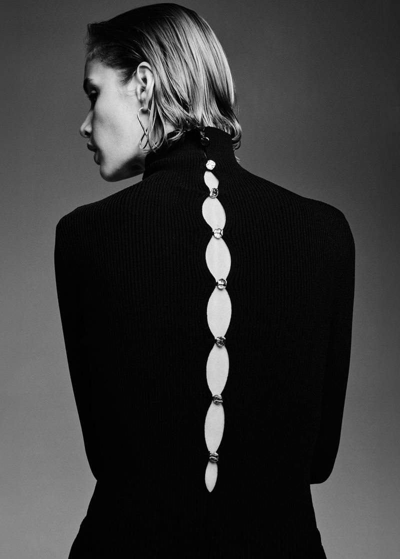 Monochrome fashion portrait of a woman with short blonde hair in a black turtleneck sweater with back cutout and silver chain.