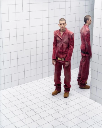 Young adult man in a matching red-burgundy jacket and pants, standing in a white tiled corner studio with a mirrored duplicate figure.