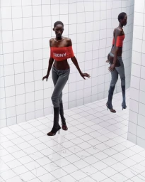 Model in a red off-the-shoulder top and grey pants posing inside a curved white tiled room with a mirror reflection.