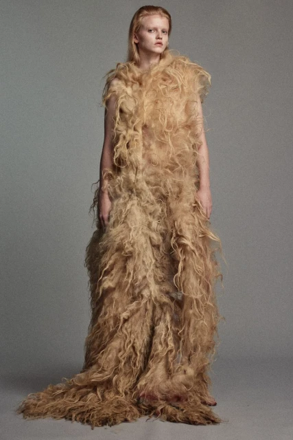 Fashionable woman wearing long, fuzzy, tan coat in studio shot. Stylish outerwear and blonde hair. Full-length fashion studio portrait.
