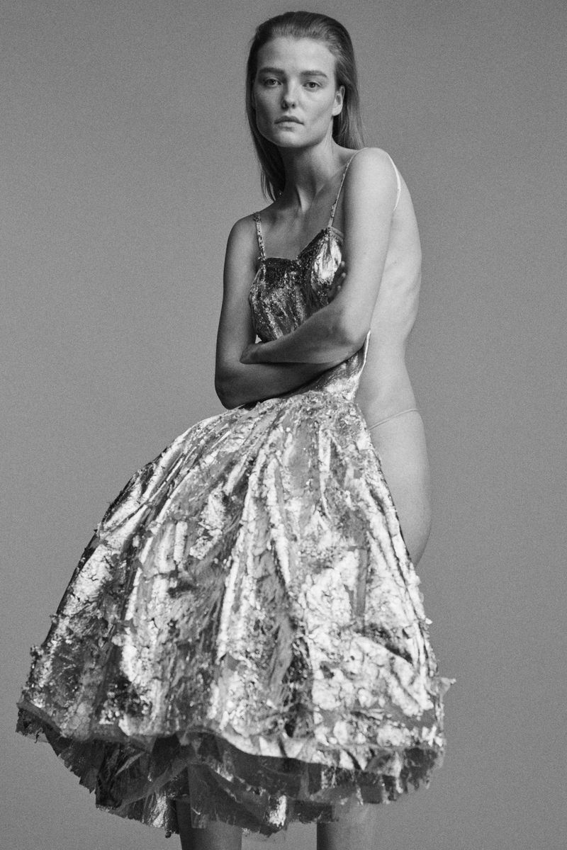 Model wearing a structured metallic silver dress against a neutral grey studio background for Ponte S/S 25 lookbook.