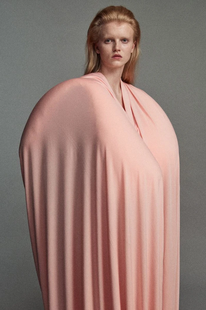Model wearing voluminous pink draped garment against a plain grey studio background for Ponte S/S 25 Lookbook