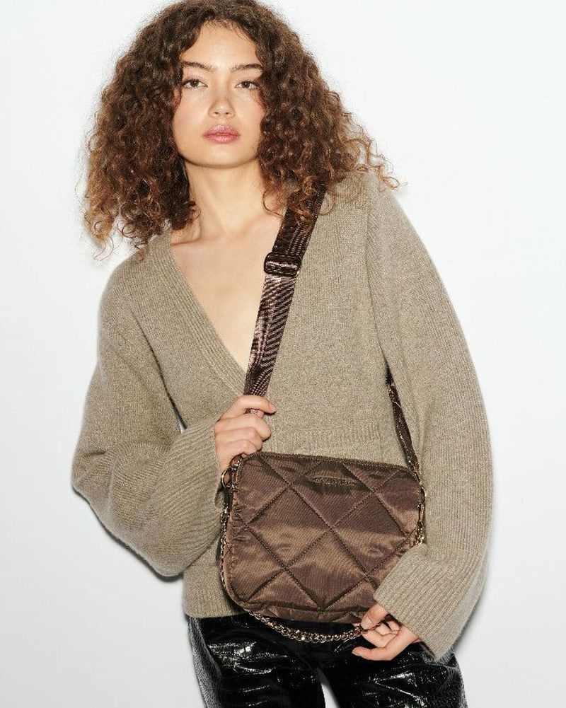 Fashionable woman posing with a quilted crossbody bag in studio setting, wearing a cozy V-neck sweater and shiny black pants.