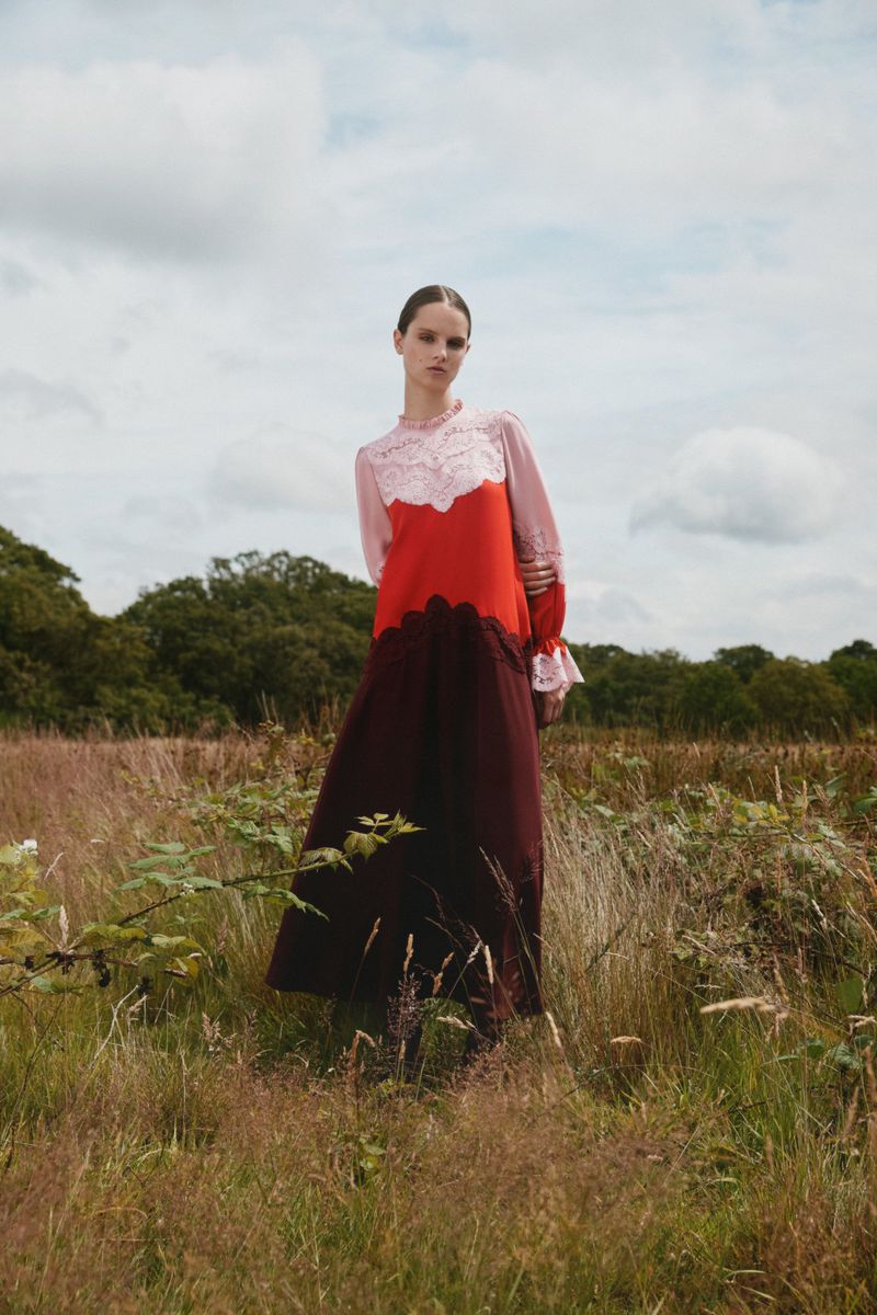 Model standing in a tall grass meadow wearing a color-blocked long-sleeve dress against an overcast sky.