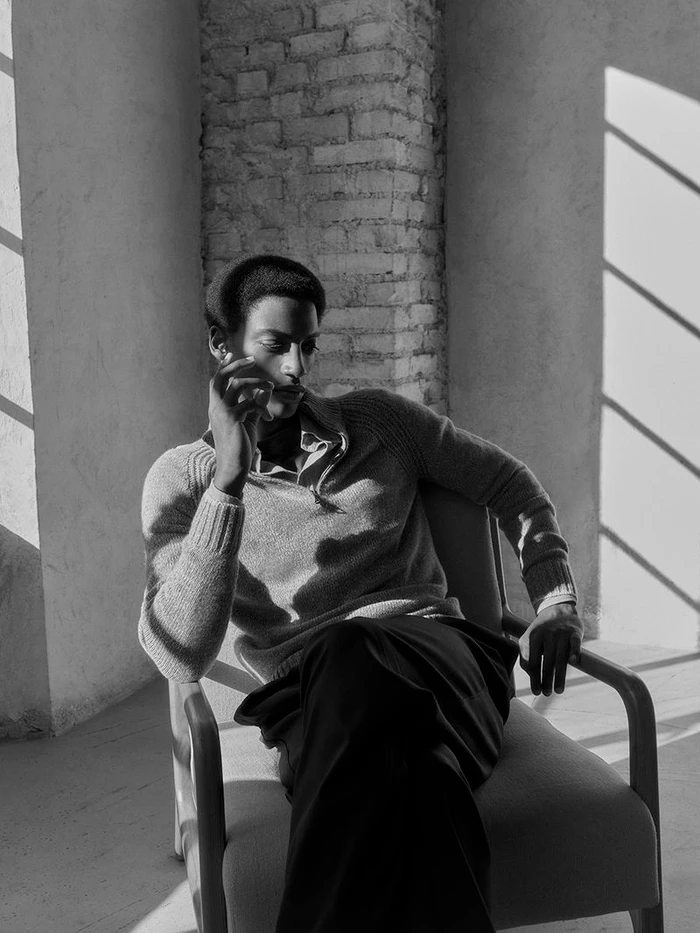 Black man in a knitted sweater seated in a chair, captured in high-contrast monochromatic lighting for Paul and Shark