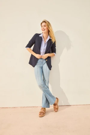 Model in dark blazer and light blue jeans leaning against a plain wall for J. McLaughlin catalogue