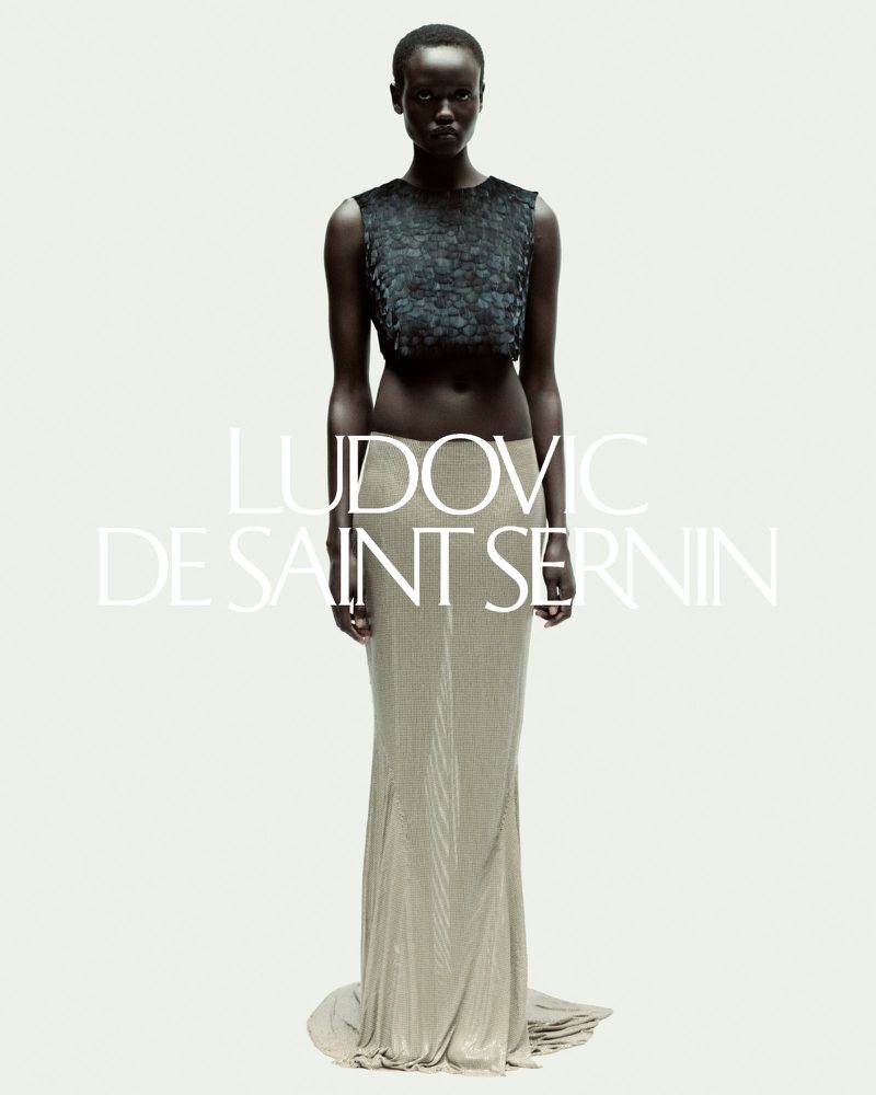 Elegant Black model poses in a green sequined crop top and a shimmering gold skirt in a fashion photo against a white backdrop.