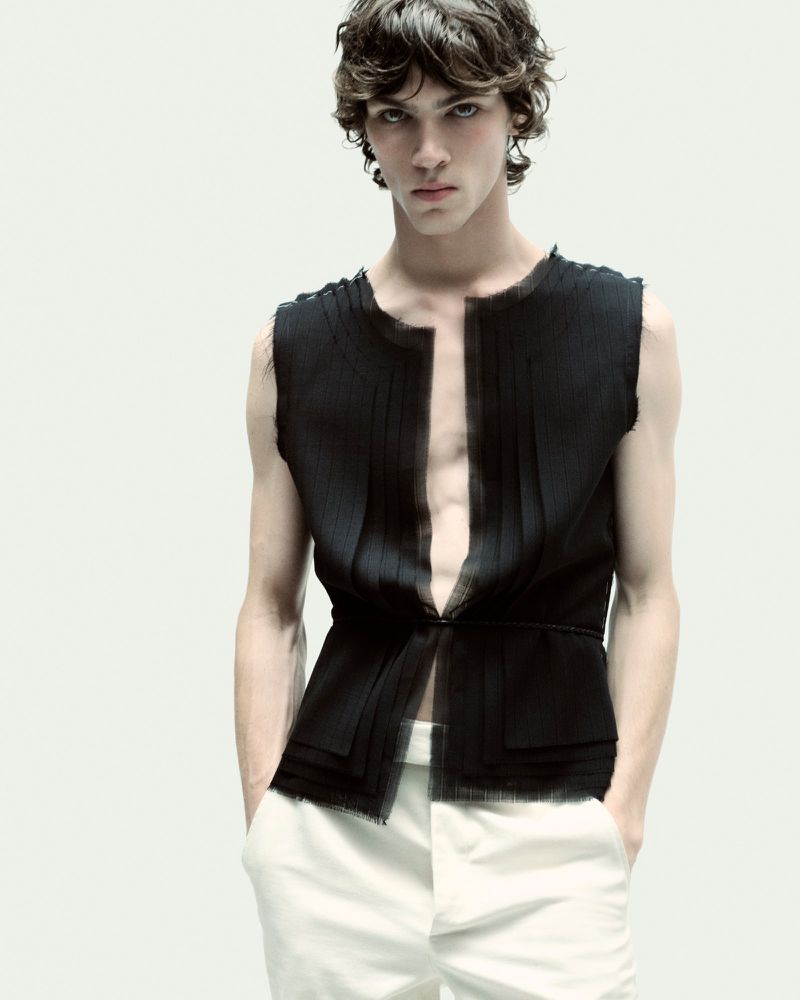 Model wearing a black sleeveless top and white trousers against a plain light background