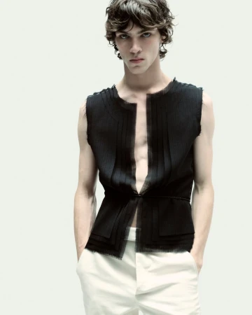 Model wearing a black sleeveless top and white trousers against a plain light background