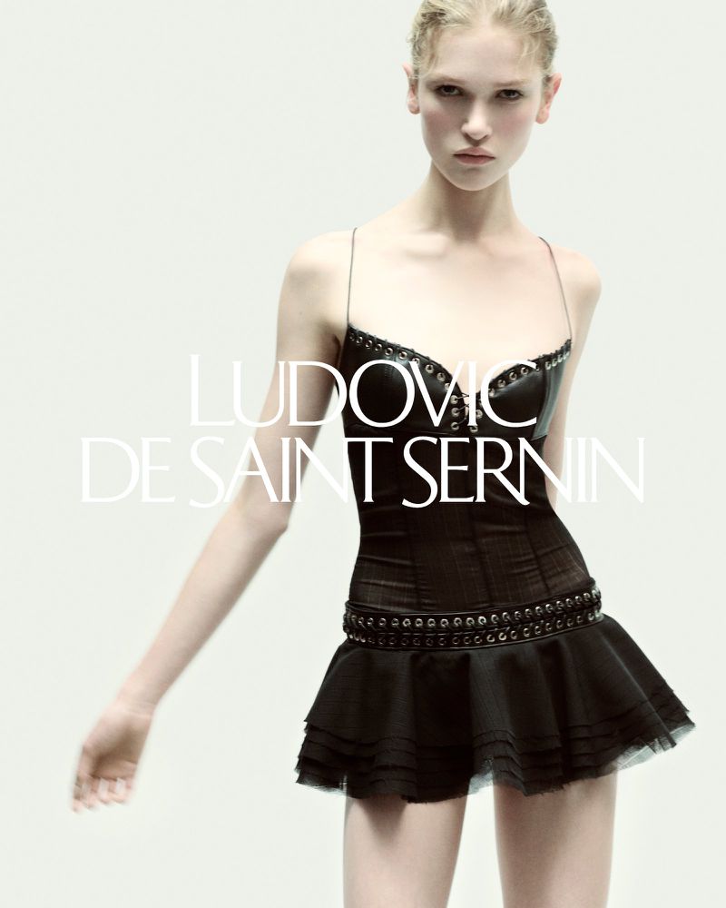 Fashion shot of a female model wearing a black bodice and skirt. The image features text overlay: LUDOVIC DE SAINT SERNIN.