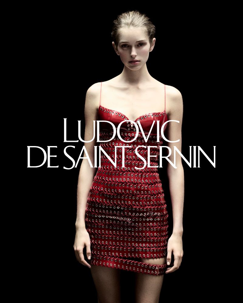 Fashion shot of a woman in a red dress by Ludovic de Saint Sernin against a black background, showcasing beauty and style in a studio setting.