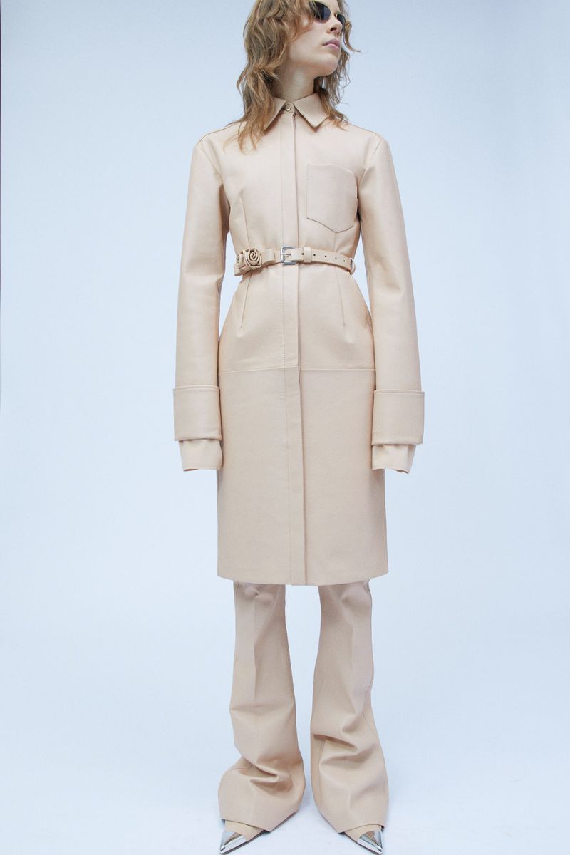 Model wearing a neutral beige leather coat and matching trousers against a clean white seamless background.
