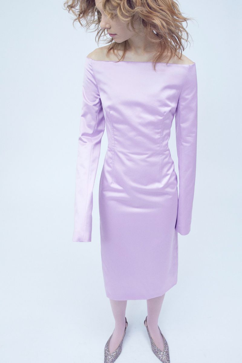 Woman in lavender off-the-shoulder long-sleeved dress and silver flats, captured in a full shot against a light backdrop, fashion editorial.