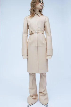 Model wearing a neutral beige leather coat and matching trousers against a clean white seamless background.