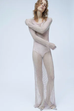 Model in a sheer mesh crystal dress posing against a plain light grey studio backdrop for Sportmax