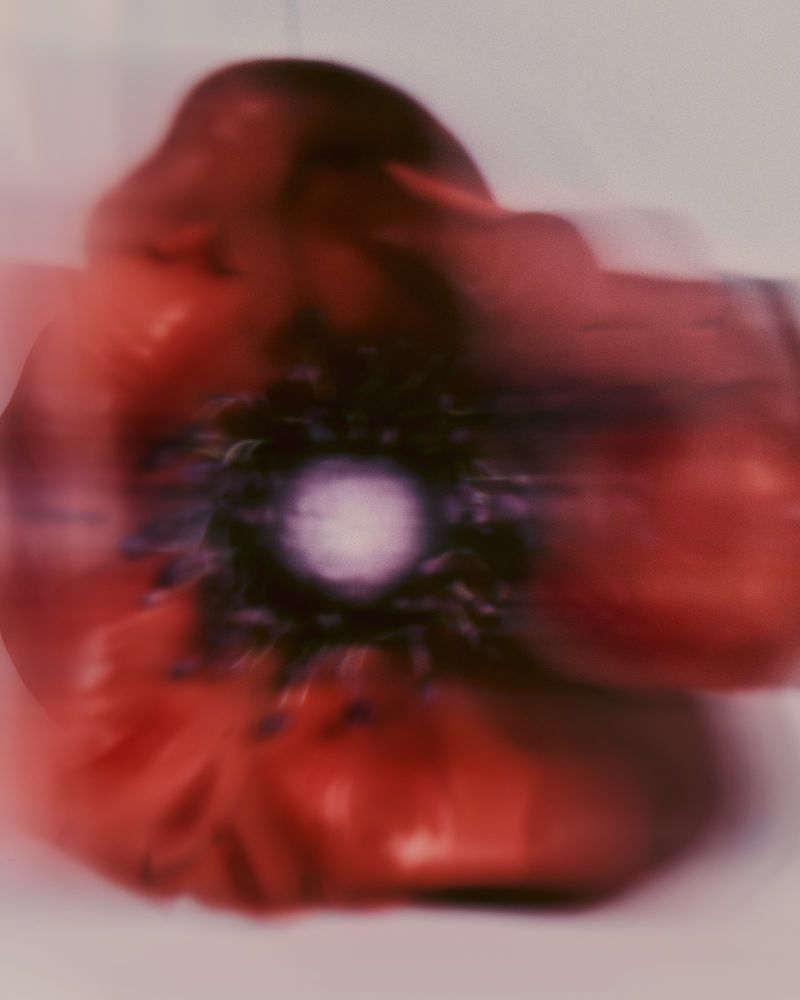 Motion-blurred abstract close-up of a red poppy flower bloom against a pale background.