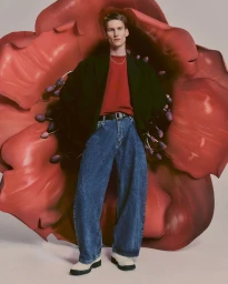 Model standing in front of an oversized red flower sculpture wearing a dark blazer, red top, and denim jeans