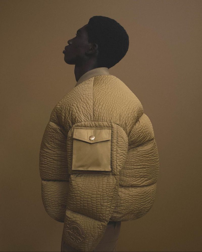 Profile shot of a Black male model with afro wearing a textured puffer jacket against a neutral backdrop in a fashion editorial setting.