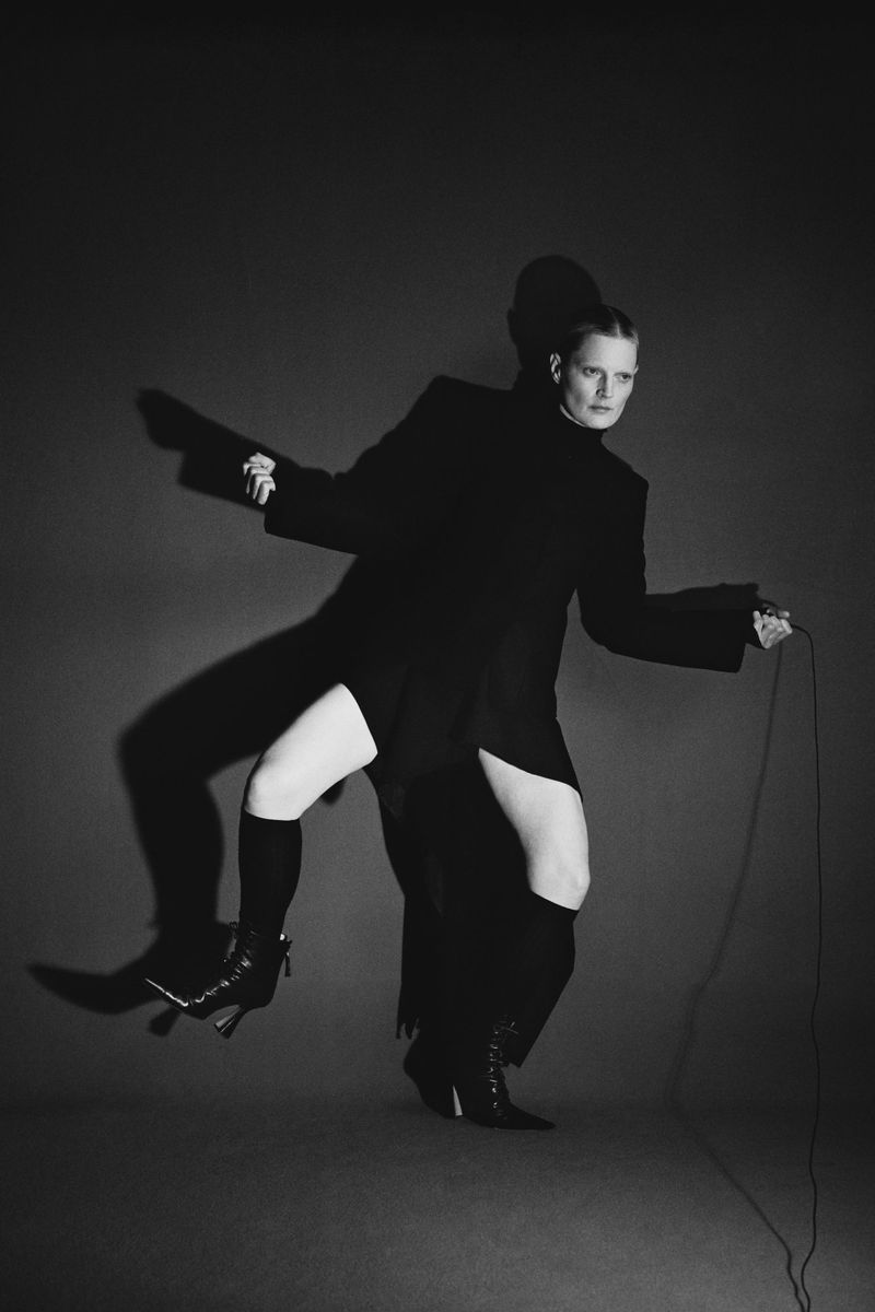 Model in black coat holding a cord against a dark backdrop in a monochrome fashion lookbook portrait