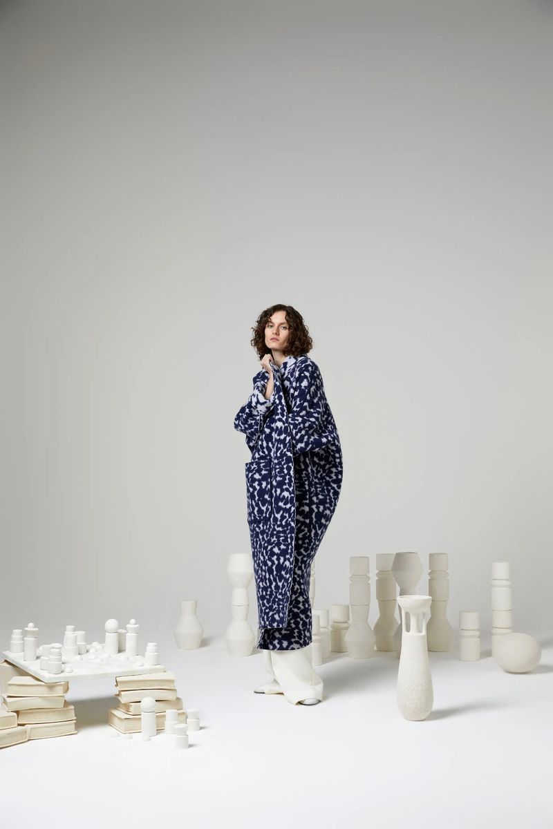 Adult woman in a patterned robe poses in a bright studio with chess and pottery. Indoor studio lighting, fashion, style, and unique design.