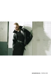 Model wearing a black leather jacket and black dress posing against an industrial concrete wall for Boyarovskaya Fall Winter 2024.