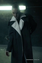 Model wearing an oversized dark coat with structured white lapels standing beneath a fluorescent light in a dark space.