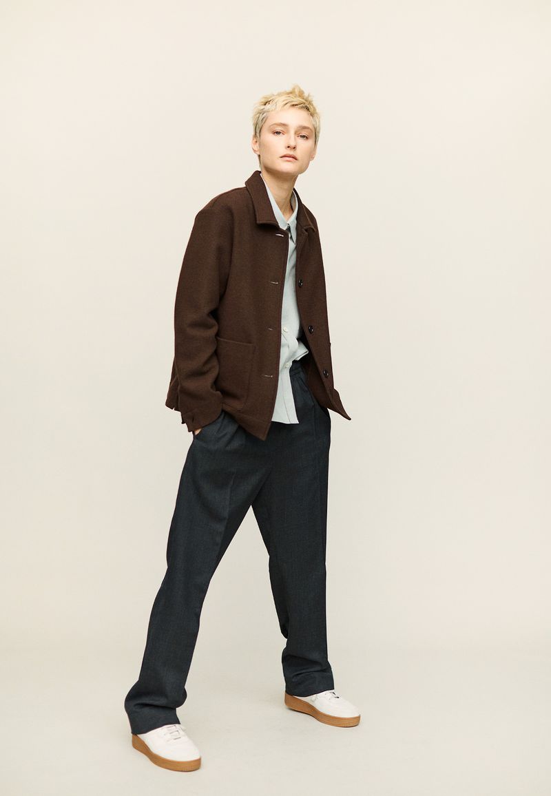 Woman in brown jacket and dark pants posing in a studio with a neutral background. Fashion editorial shot in a well-lit studio.