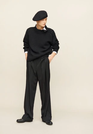 Adult female model in a full-length studio portrait wearing a black sweater, black trousers, black shoes and a black beret, looking to the side.