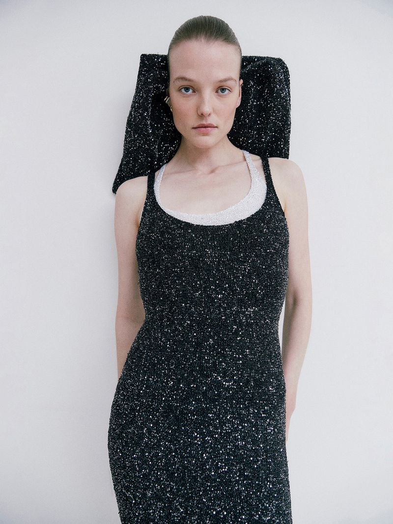 Elegant woman in a sparkling black dress with an architectural headpiece posing in a bright studio with soft, diffused lighting.