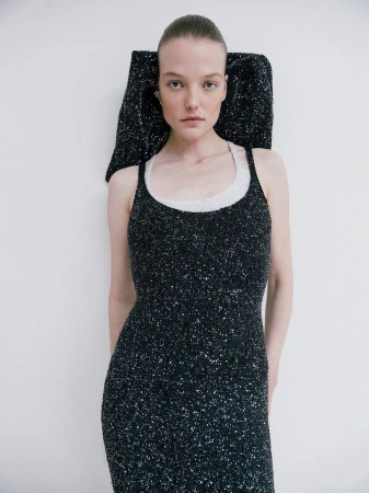 Elegant woman in a sparkling black dress with an architectural headpiece posing in a bright studio with soft, diffused lighting.