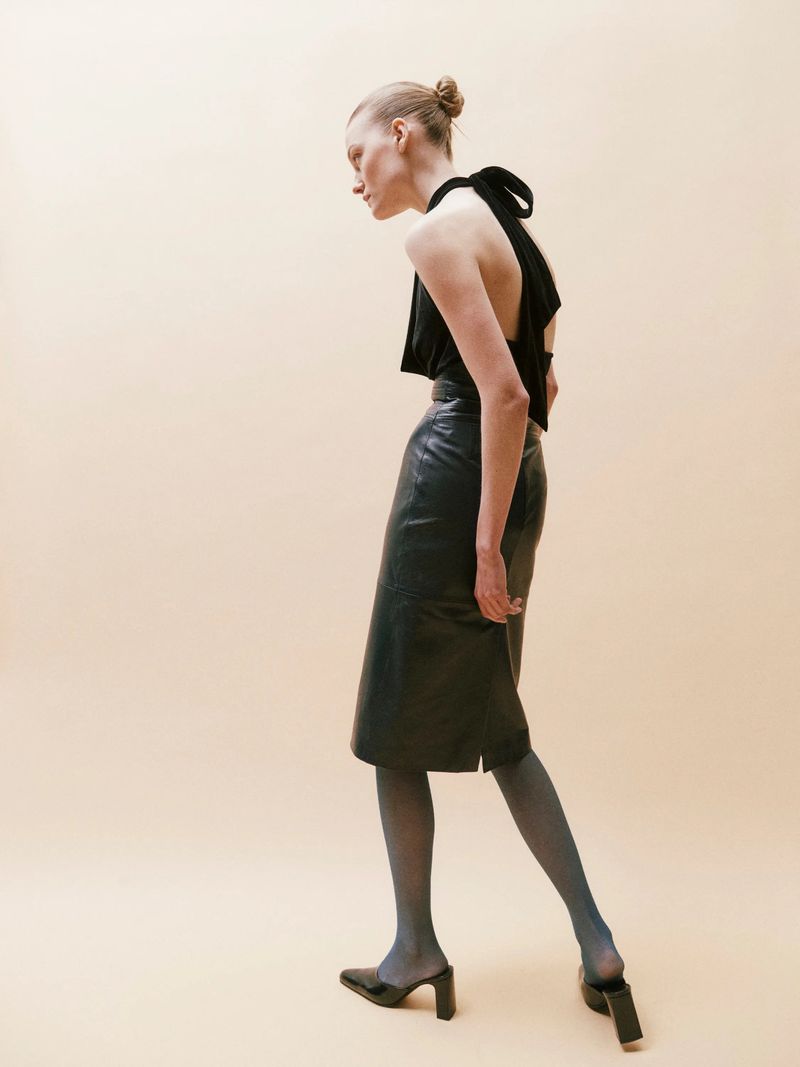 A woman poses in a long-sleeved, short black Hervé Léger dress in a studio setting, highlighted by dynamic lighting and a dark backdrop.