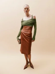 Model wearing an olive green draped off-shoulder top and a brown leather pencil skirt against a solid neutral backdrop.