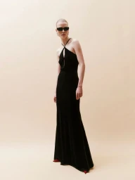 Roos Abels poses in a black halter evening gown and dark sunglasses against a warm beige backdrop for Hervé Léger.