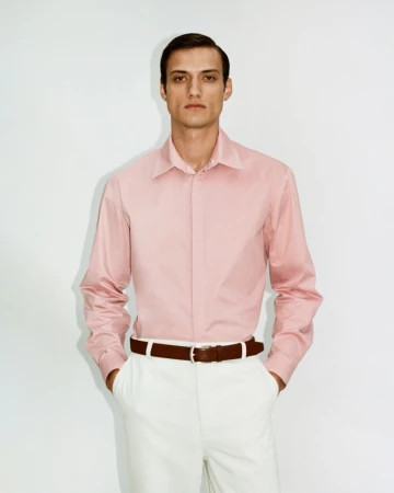 Model wearing a pink button-down shirt and white trousers with a brown belt against a plain white background