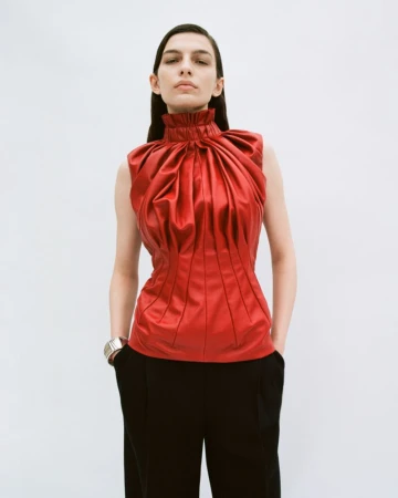 Model in a structured red high-neck top and black trousers against a neutral white seamless background.