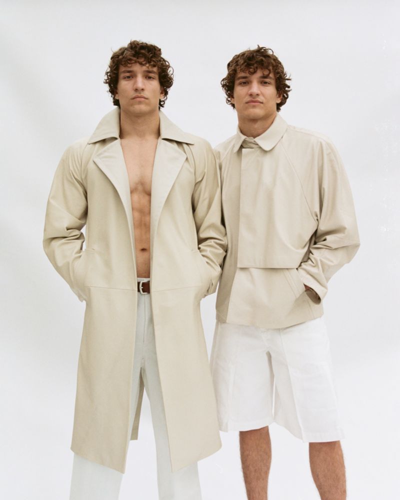Two adult males pose against a white background, one wearing a beige trench coat and white pants, the other a beige jacket and shorts.