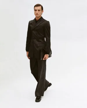 Model in dark pinstripe suit and black shoes carrying a portfolio against a white seamless background