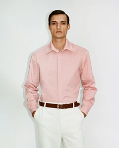 Model wearing a pink button-down shirt and white trousers with a brown belt against a plain white background