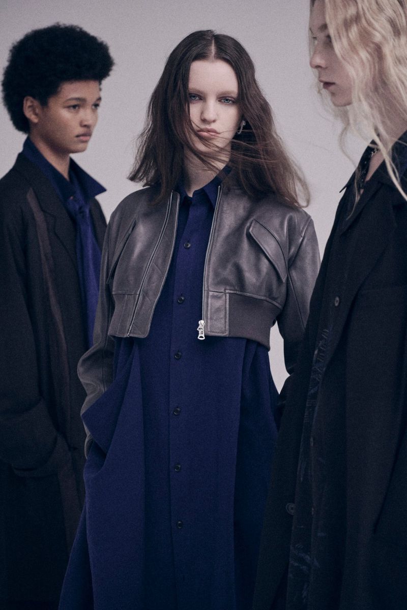 Fashion editorial featuring three slender individuals of mixed ethnicity wearing navy blue and black outerwear in a neutral studio setting.