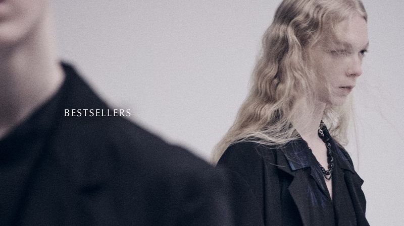 Fashion portrait of a blonde woman in a black jacket looking away next to a blurred figure and the text “BESTSELLERS” on a white background.