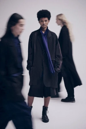 Three models wearing dark Yohji Yamamoto S'YTE clothing against a white seamless background with motion blur effects.