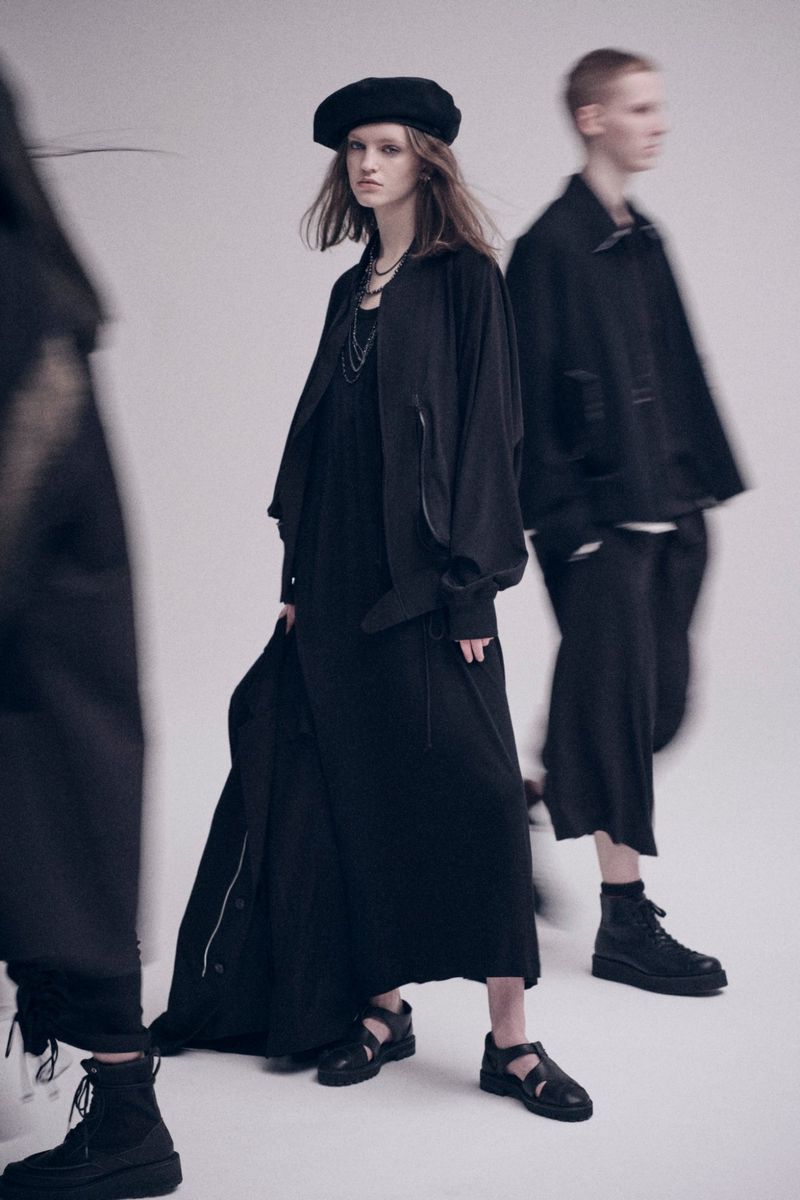 Three people in black clothing walking in a studio: an adult woman in a dress and jacket is in focus; two more are blurred.