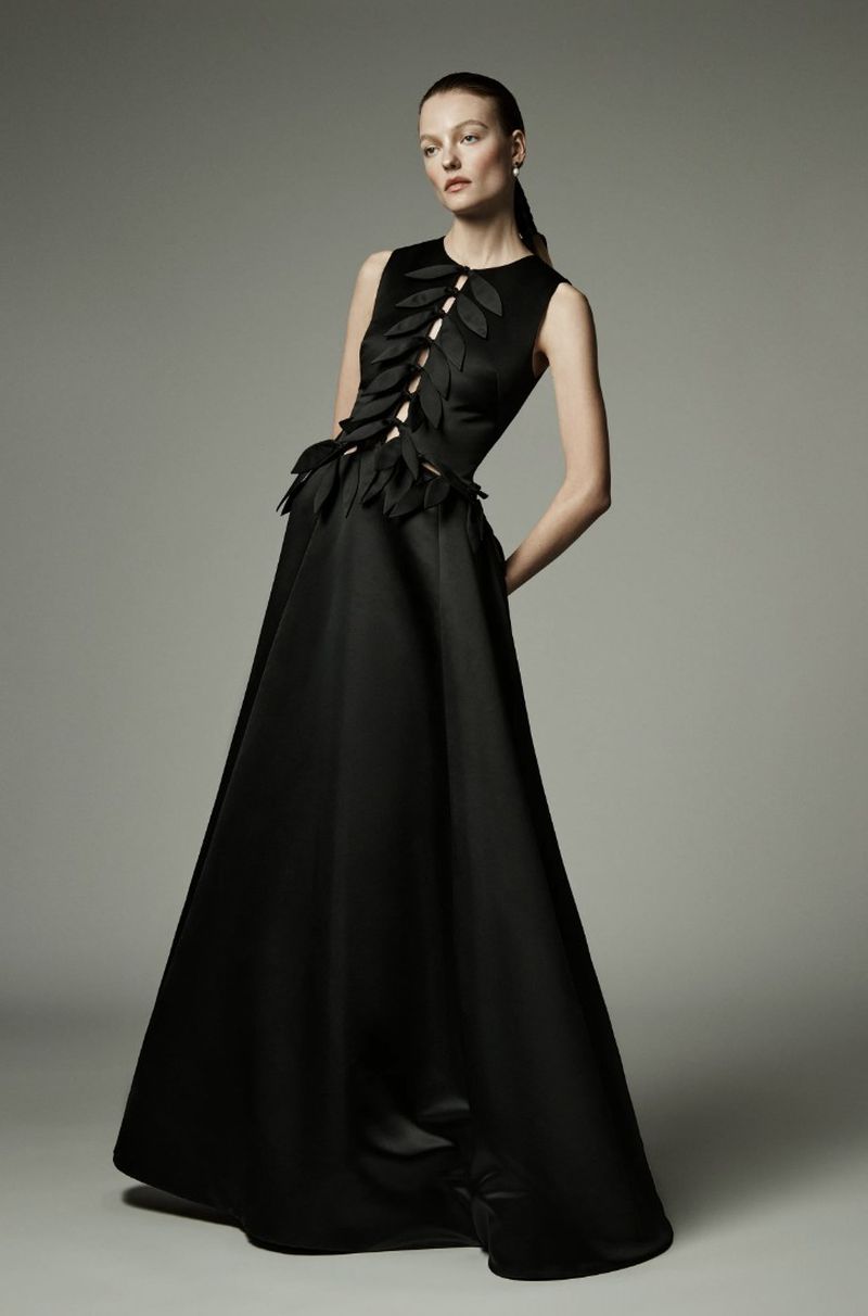 Elegant woman in a black sleeveless gown with leaf-like adornments posing in a photo studio, fashion and elegance concept.