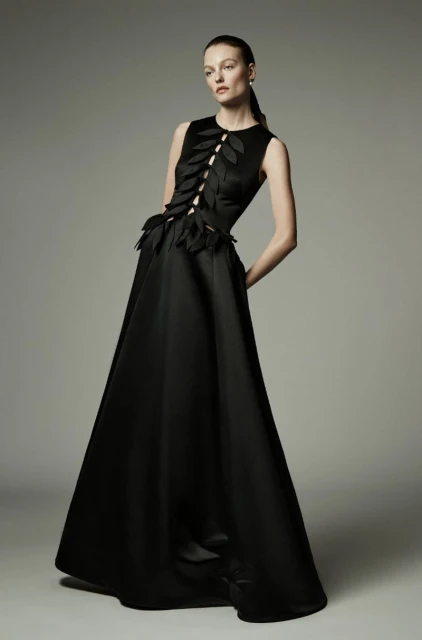 Elegant woman in a black sleeveless gown with leaf-like adornments posing in a photo studio, fashion and elegance concept.