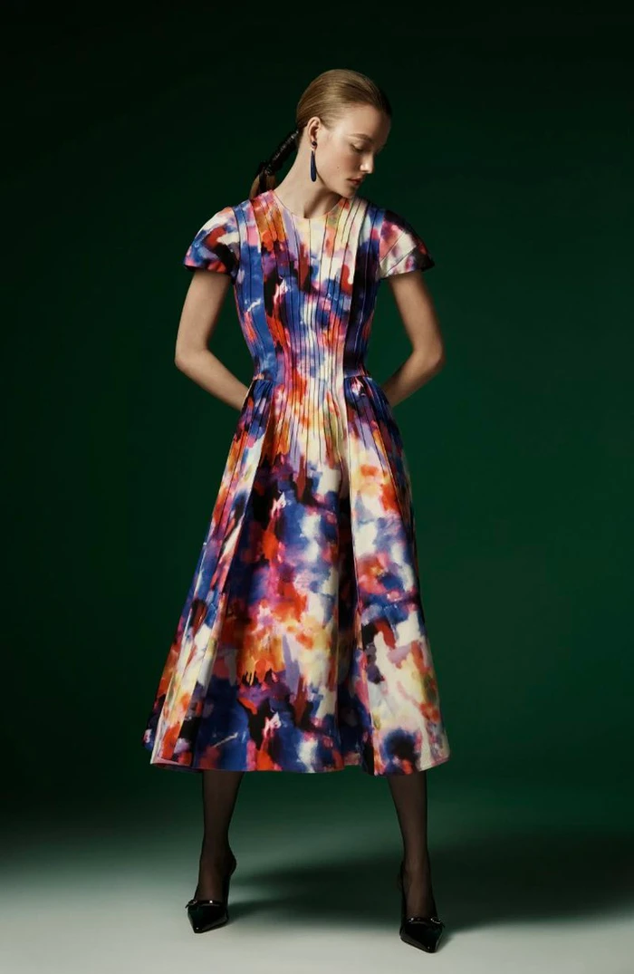 Model Roos Abels in a colourful patterned midi dress against a dark green studio backdrop for Jonathan Cohen FW24 lookbook.