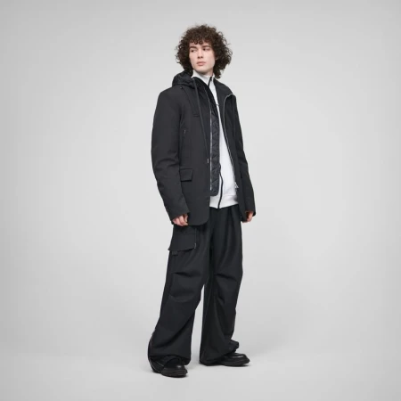 Model wearing a layered black jacket and wide-leg black cargo trousers against a neutral grey studio backdrop.