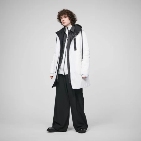 A young adult male model with curly brown hair poses in a white puffer coat and black pants against a light grey studio backdrop.
