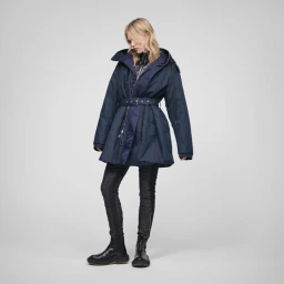 Model wearing a belted navy hooded jacket with dark fitted trousers and boots against a light grey studio background.