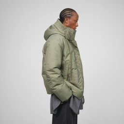 Model in profile wearing an olive green puffer jacket and grey top against a grey seamless background