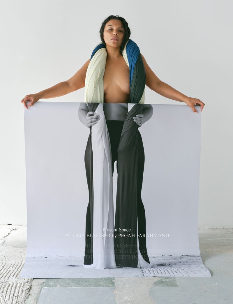 Person partially nude, wearing textured scarf, standing behind black and white photograph of body wearing matching fabric.